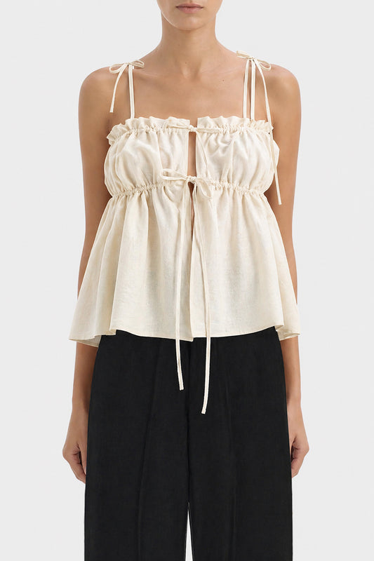 A model wearing a cream-colored ruffled top with straps and black wide-leg trousers, shown from the neck down against a light gray background.