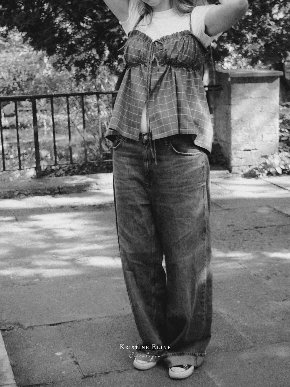 Person wearing a grey checkered ruffle top and wide-leg jeans standing outdoors.