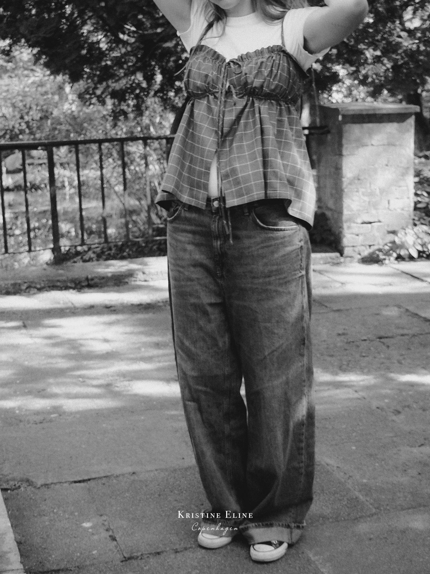 Person wearing a grey checkered ruffle top and wide-leg jeans standing outdoors.