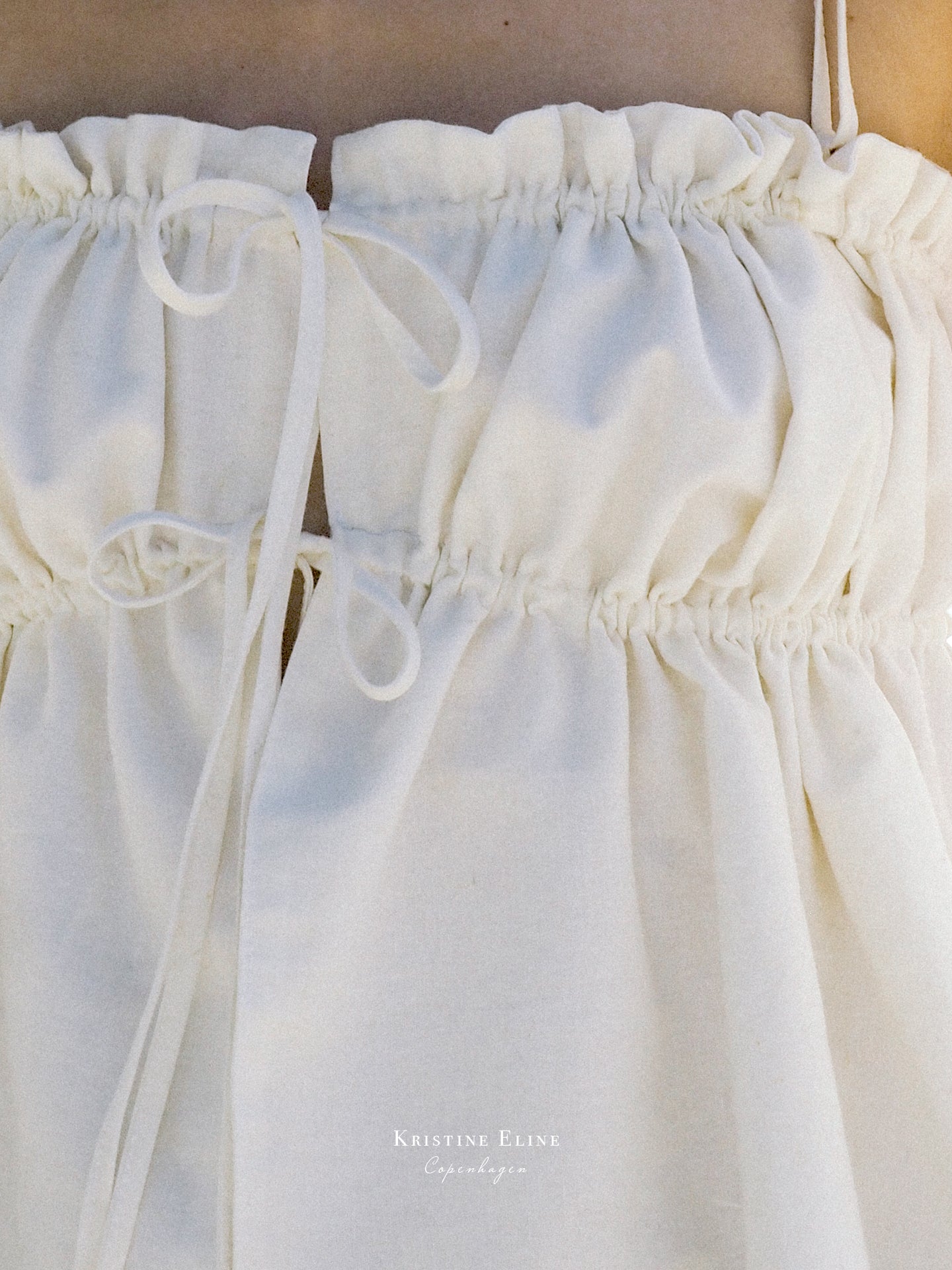 Close-up of a white cotton and linen top with ribbons and a brand name on top