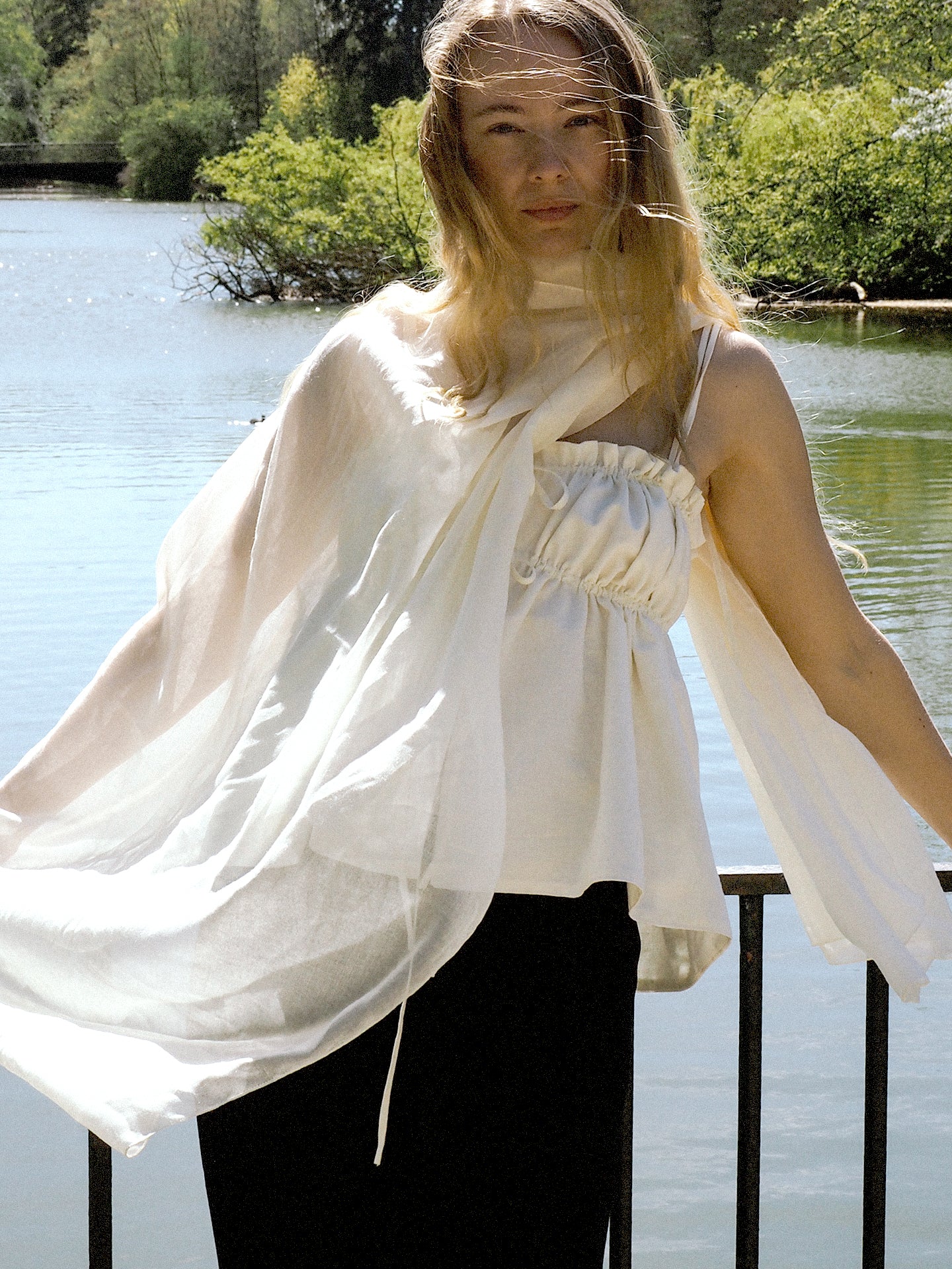 Woman wearing a ivory top with with a flowing scarf in front of a river