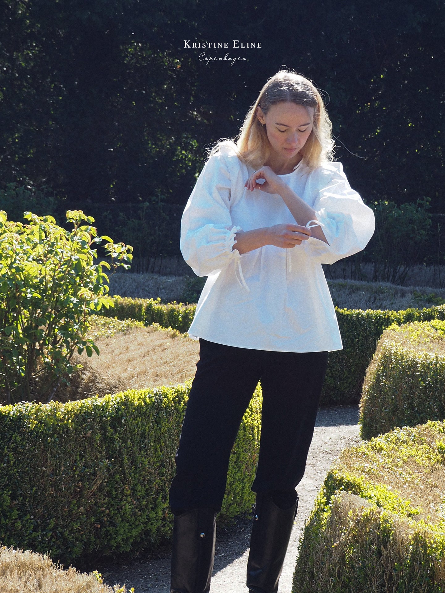 Woman in a White Panel Blouse and black pants standing in a garden