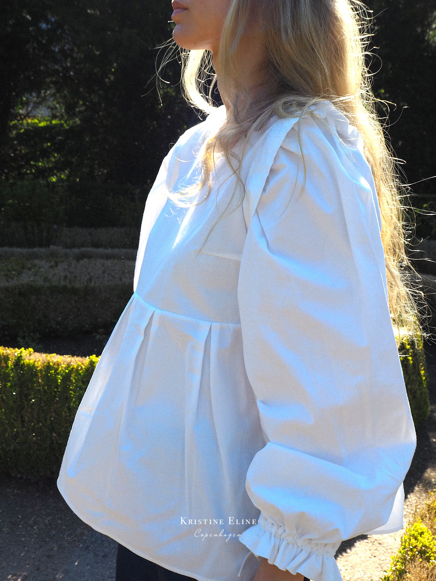 Woman wearing a white blouse with long puffed sleeves in an outdoor setting